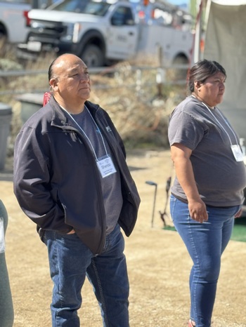 TBB 16 Kevin Shendo Kevin Shendo JNET director stands looking at on off camera demo with his hands in jeans pockets standing next to a JNET technician in training with a utility truck in the background