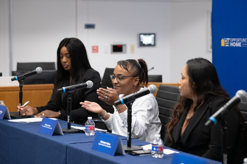 Belinda Parker-Mendoza sits in the middle of a table behind a microphone along with three other panelists 