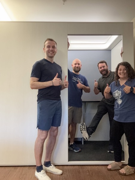 Crew of NEK volunteers gives thumbs standing in doorway of privacy pod
