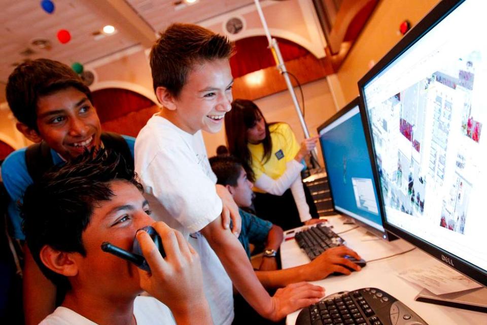 Three students smiling gleefully while looking at computer screen in classroom while working on a science project